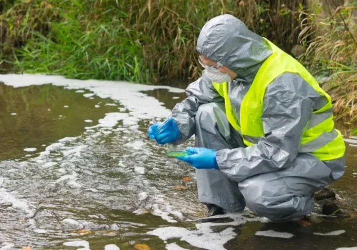 scientist in a protective suit and mask, collects legionella samples from the pond in a Petri dish